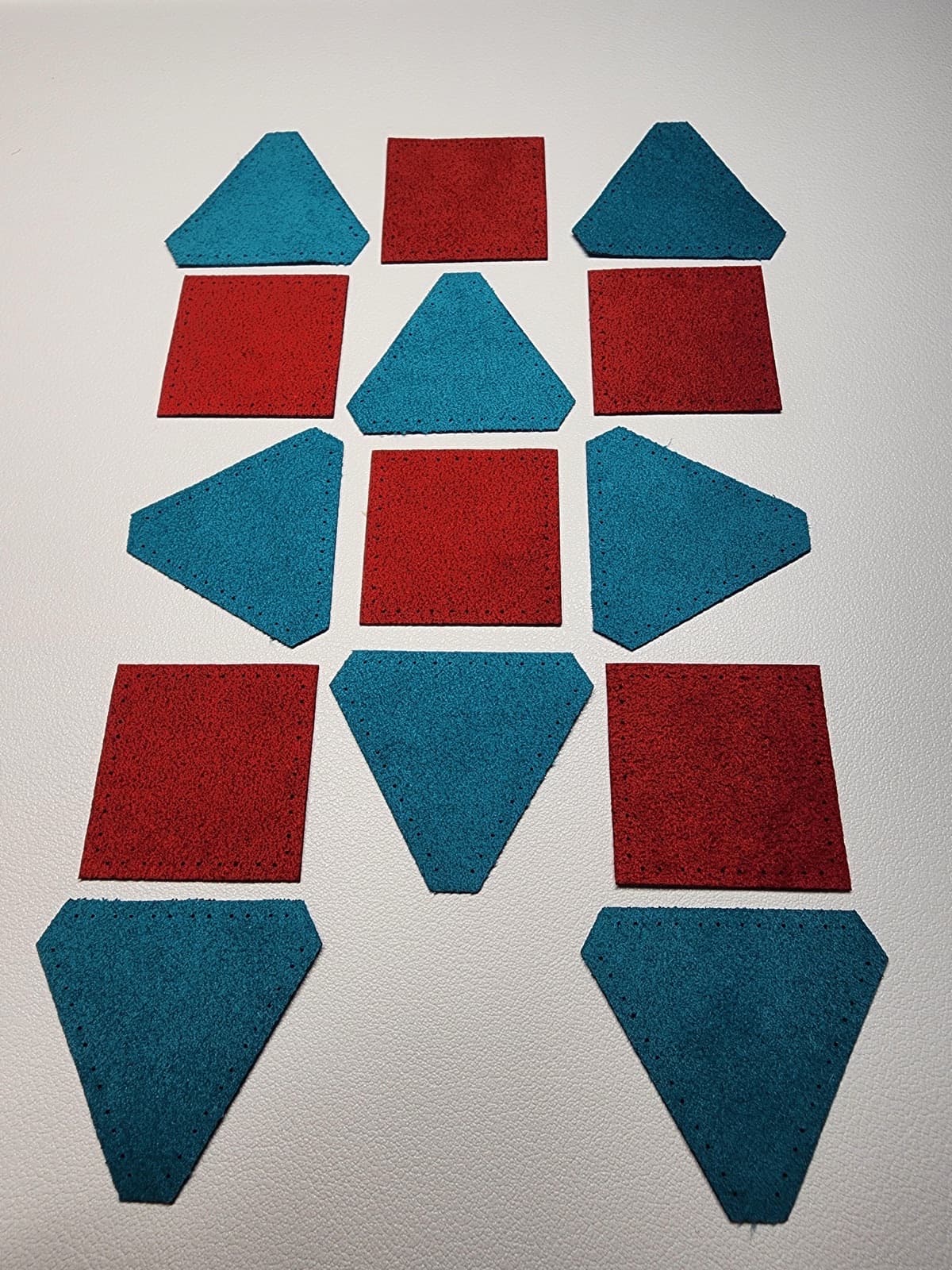 Fourteen precut Ultrasuede panels in red and teal, laser-cut stitch holes visible along every edge