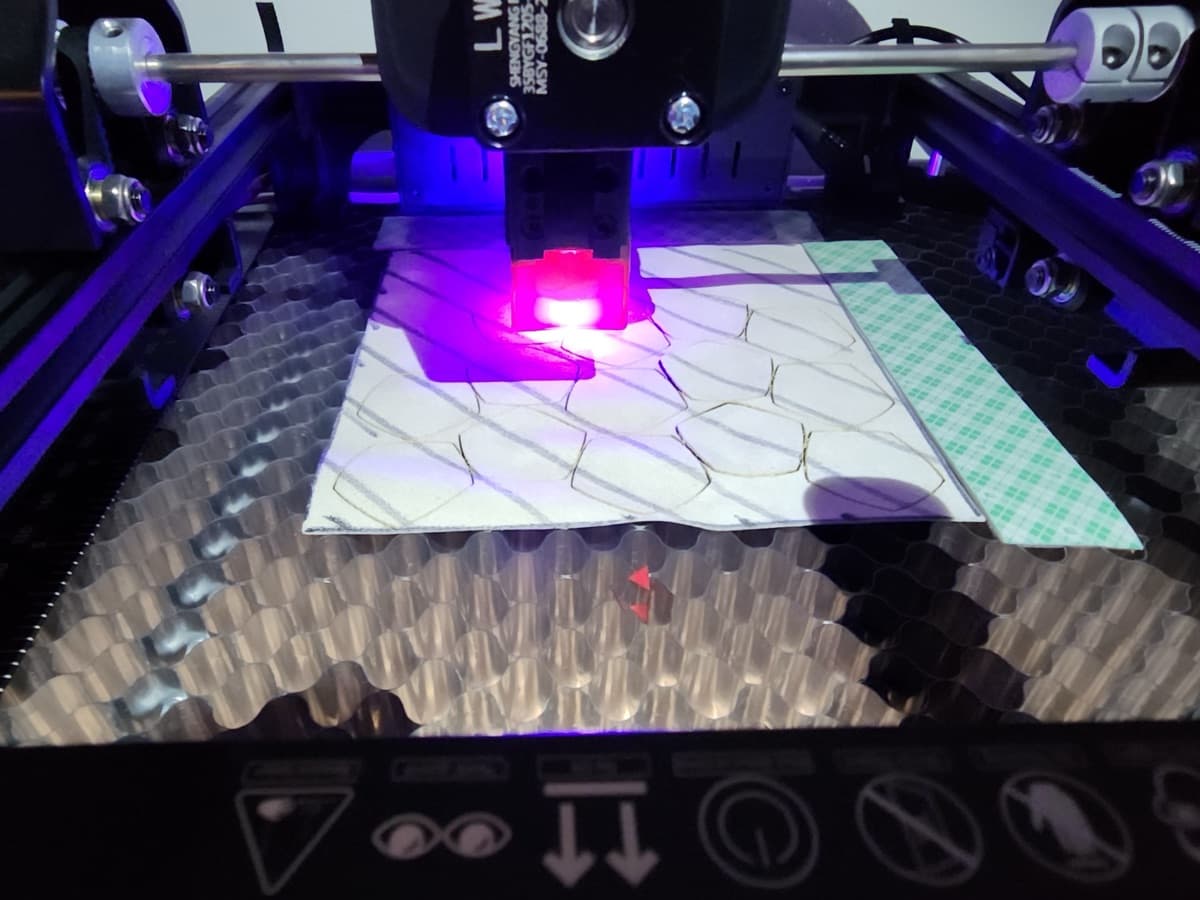 A diode laser cutting hexagonal footbag panels out of a sheet of suede